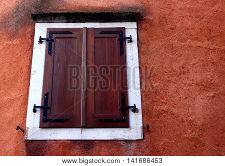 A modern wooden dark brown closed window with white frame on a red wall