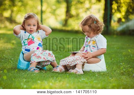 The two little baby girls two-year old sitting on pots against green grass