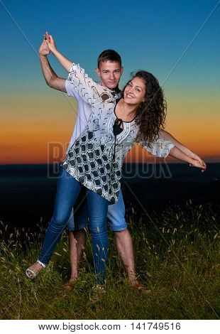young romantic couple open arms and having fun at sunset on outdoor, beautiful landscape and dark sky, love tenderness concept, young adult people