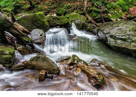 small cascades on the forest river among huge bouders covered with moss