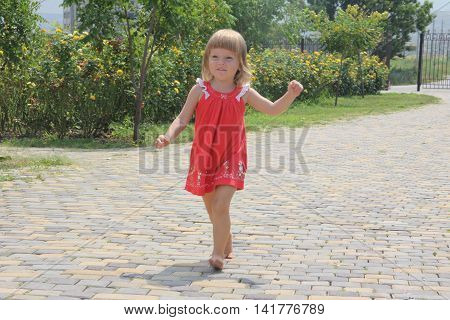 little cheerful girl running barefoot on the road on the street in summer