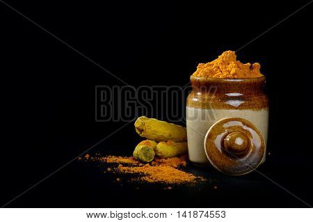 Turmeric powder in clay pot with roots or barks on black background