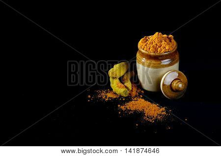 Turmeric powder in clay pot with roots or barks on black background