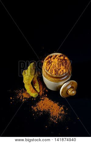 Turmeric powder in clay pot with roots or barks on black background