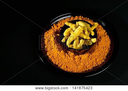 Turmeric powder and roots or barks on black background
