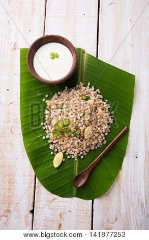 Sabudana Khichadi - An authentic dish from Maharashtra made with sago seeds served over coconut leaf with curd in a wooden bowl