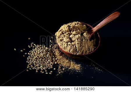 Coriander Powder in wooden bowl with seeds on black background