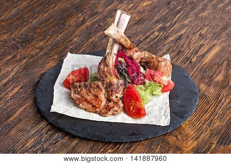 ribeye steak on the bone tomahawk served with tomatoes and iceberg lettuce on pita on slate board.