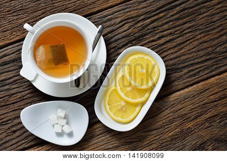 Top view of cup of tea with tea bag, sugar cube and lemon on wooden table