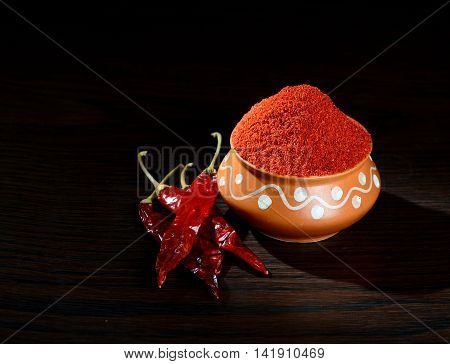chilly powder in clay pot with red chilly, dried chillies on wooden background