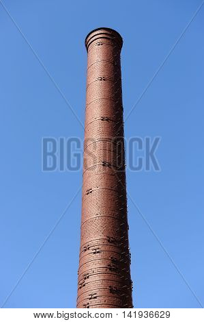 An old red brick factory chimney against a blue sky background