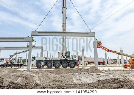 Mobile crane is operating and worker is assembly concrete joist in high place. Height worker is placing truss on building skeleton.