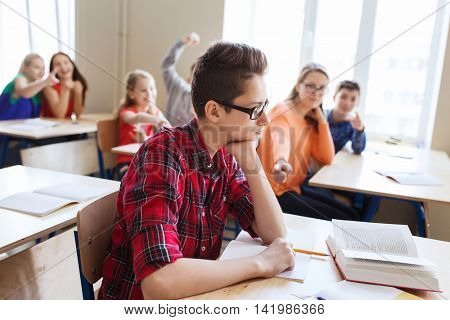 education, bullying, conflict, social relations and people concept - student boy in glasses reading book and suffering of classmates mockery at school