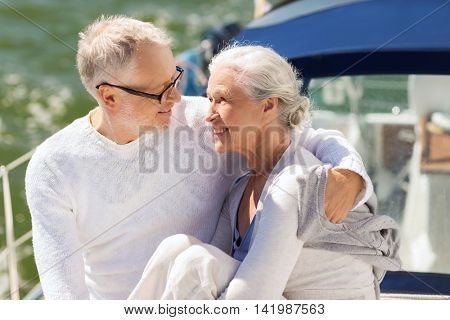 sailing, age, tourism, travel and people concept - happy senior couple hugging on sail boat or yacht deck floating in sea
