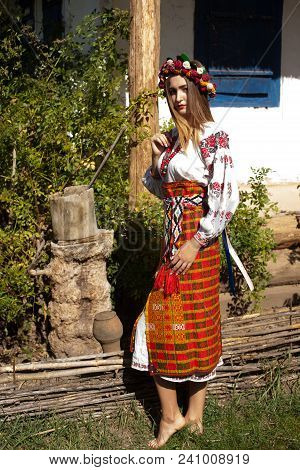 Beautiful Ukrainian Girl In National Clothes Embroidered On A Wooden Hut In The Summer