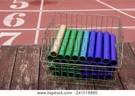 A Basket Of Colorful Relay Batons Are On A Wood Overhang Above The Comon Start Line Of A Track.