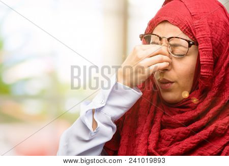 Young arab woman wearing hijab with sleepy expression, being overworked and tired, rubbes nose because of weariness