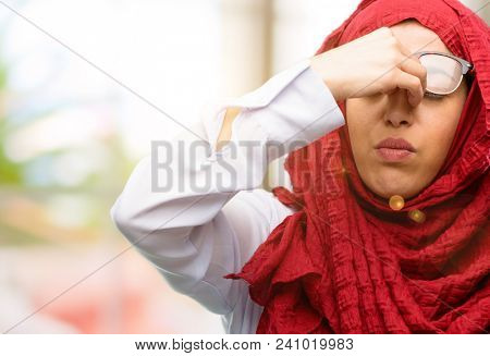 Young arab woman wearing hijab with sleepy expression, being overworked and tired, rubbes nose because of weariness