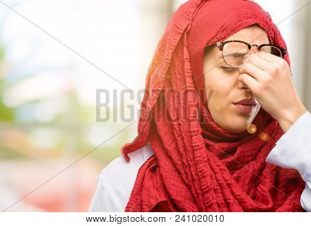 Young arab woman wearing hijab with sleepy expression, being overworked and tired, rubbes nose because of weariness