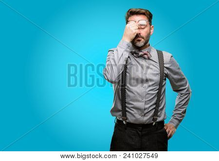 Middle age man, with beard and bow tie with sleepy expression, being overworked and tired, rubbes nose because of weariness