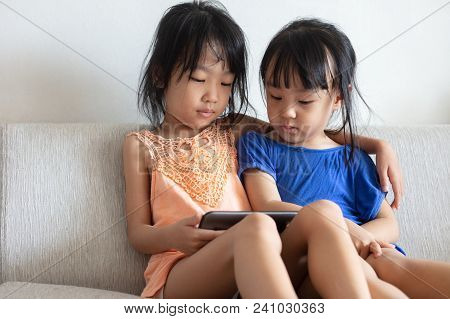 Asian Chinese Little Sisters Using Tablet On The Sofa In The Living Room