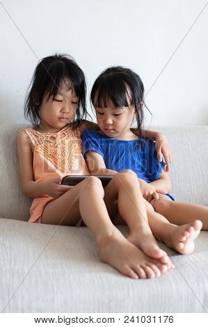 Asian Chinese Little Sisters Using Tablet On The Sofa In The Living Room