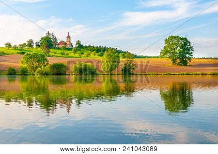 Romantic Landscape With Small Church On The Hill Reflected In The Pond. Sunny Summer Day With Blue S