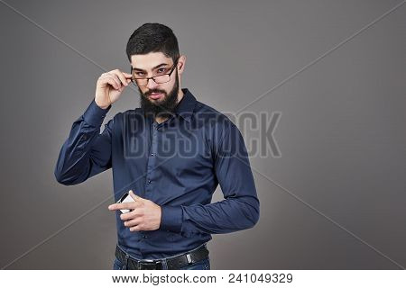 Happy Man In Glasses With Smartphone On Hands On Gray Background.