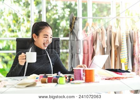 Happy Asian Smart Looking Fashion Designer Smiling And Sitting In Modern Office With Materials, Fabr