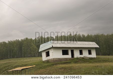 Lonely White Forgotten Building On The Green Mountain. Deep Dark Grey Sky With A Lot Of Clouds. Fore