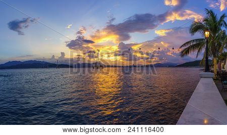 Nha Trang Bay In Sunset With Cable Car System And Street Lamp, Branches Of Coconut Tree On Foregroun