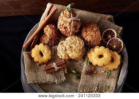 Conceptual Composition With Assortment Of Cookies, Cinnamon Sticks Bunch And Dried Oranges With Burl