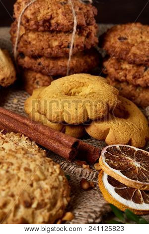 Conceptual Composition With Assortment Of Cookies, Cinnamon Sticks Bunch And Dried Oranges On A Wood