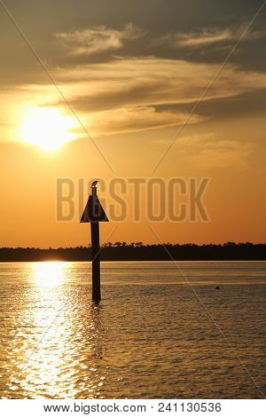 Calm Waters With Trees In The Background And Beautiful Sunset
Of Gold Reflecting From The Sky.