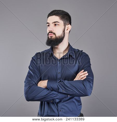Young Handsome Man With A Beard Leaning Against Grey Wall With Arms Crossed. Copy Space.