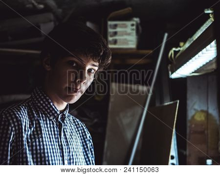 young man in checkered shirt portrait working in dark workshop