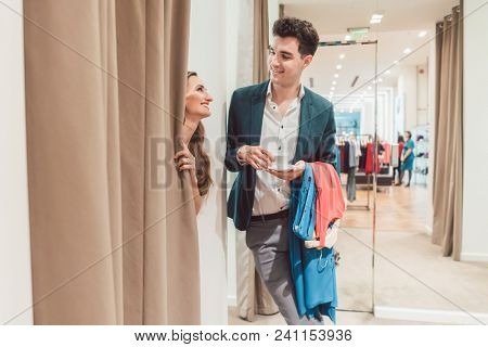 Man in fashion store waiting for his woman to appear from the fitting room being a bit bored