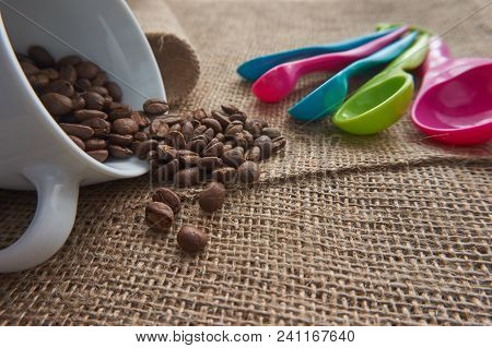 Loose Roasted Coffee Beans, White Porcelain Coffee Mug And Color Plastic Dose Measuring Spoons On Ju