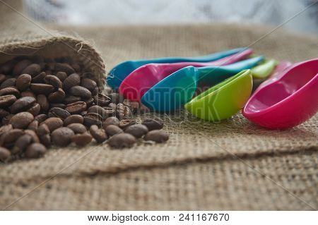 Dark Roasted Coffee Beans On Hessian Or Burlap With Colorful Plastic Kitchen Measuring Spoons In A S