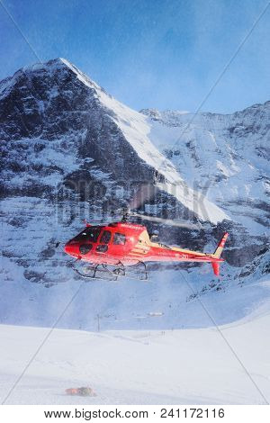 Maennlichen, Switzerland - December 31, 2013: Red Helicopter Flying In Swiss Alpine Mountain Maennli