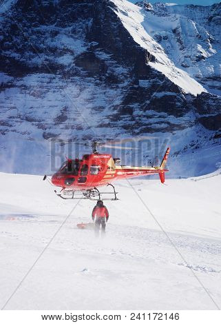 Maennlichen, Switzerland - December 31, 2013: Red Helicopter Flying Near Swiss Alpine Mountain Maenn