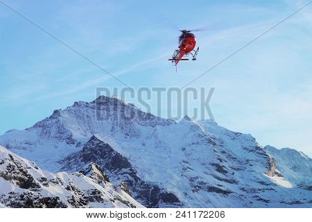 Maennlichen, Switzerland - December 31, 2013: Red Helicopter Flying In Swiss Alps Mountains Maennlic