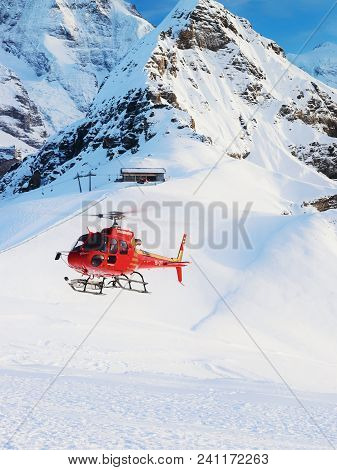 Maennlichen, Switzerland - December 31, 2013: Red Helicopter Flying In Swiss Alps Mountains Maennlic