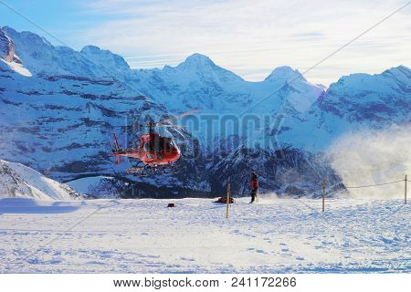 Maennlichen, Switzerland - December 31, 2013: Red Helicopter Flying At Swiss Alpine Mountains Maennl