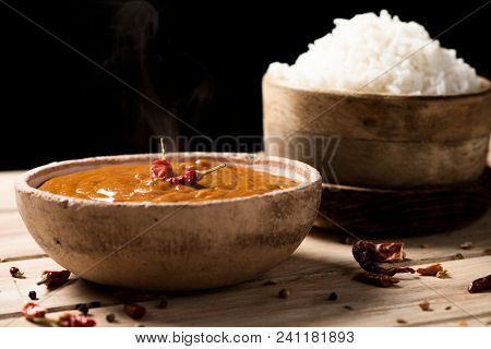 closeup of a bowl with a chicken korma curry and a bowl with cooked rice on an off-white wooden table