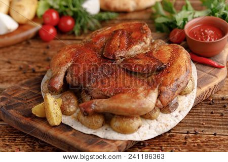 Fried Chicken On A Wooden Background With A Garnish Of Baked Young Potato. Chicken Of Tobacco. Rusti