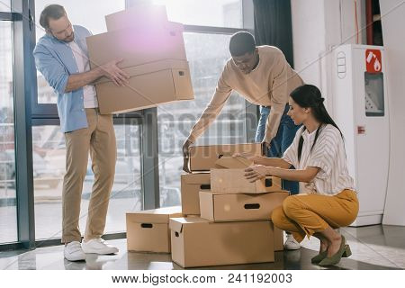 Multiracial Business Colleagues Carrying Cardboard Boxes During Relocation In New Office