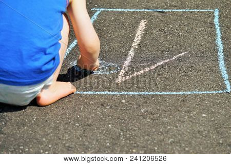 Child With Colorful Chalk In Hand On A Asphalt Road