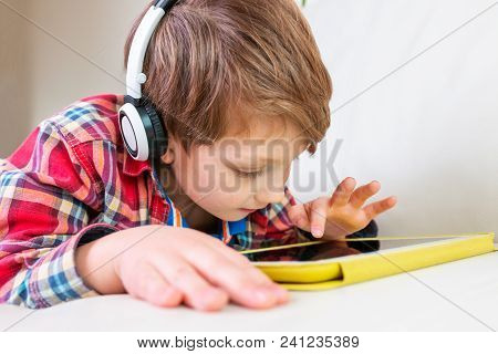 Little Boy In Headphones Laying On Bed Play The Tablet