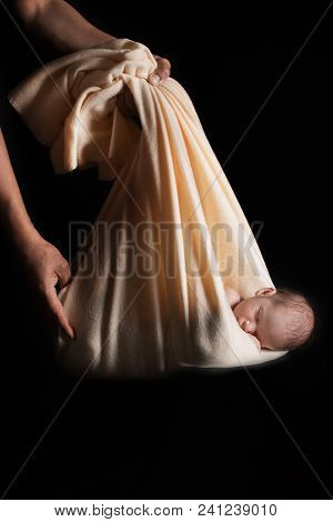 A Little Child In A Beige Cap Lies In The Sack On A Black Background